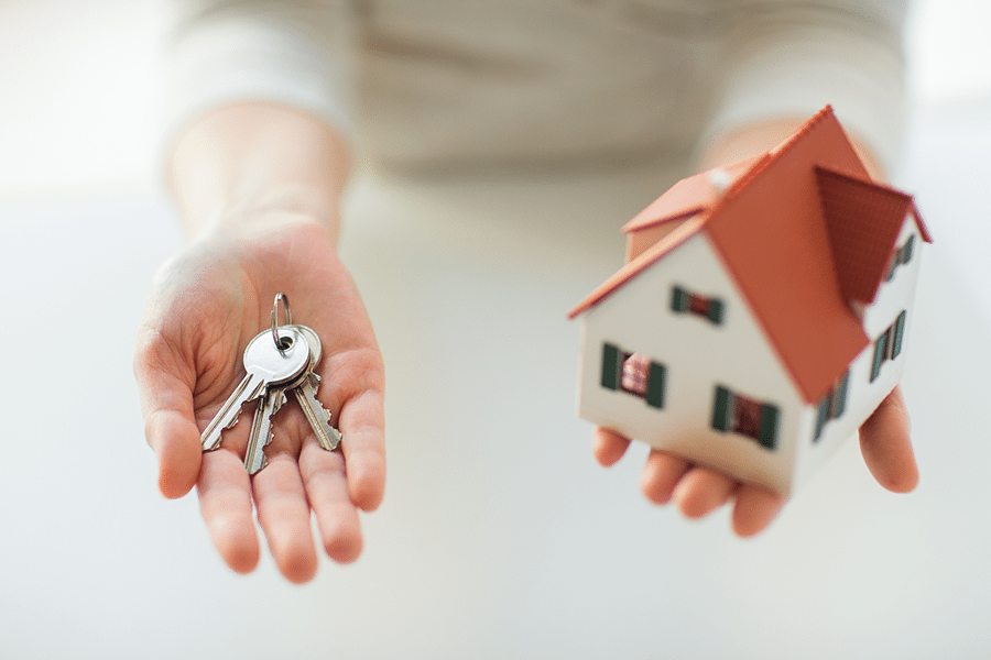 Hands holding keys and a mini model of a house.