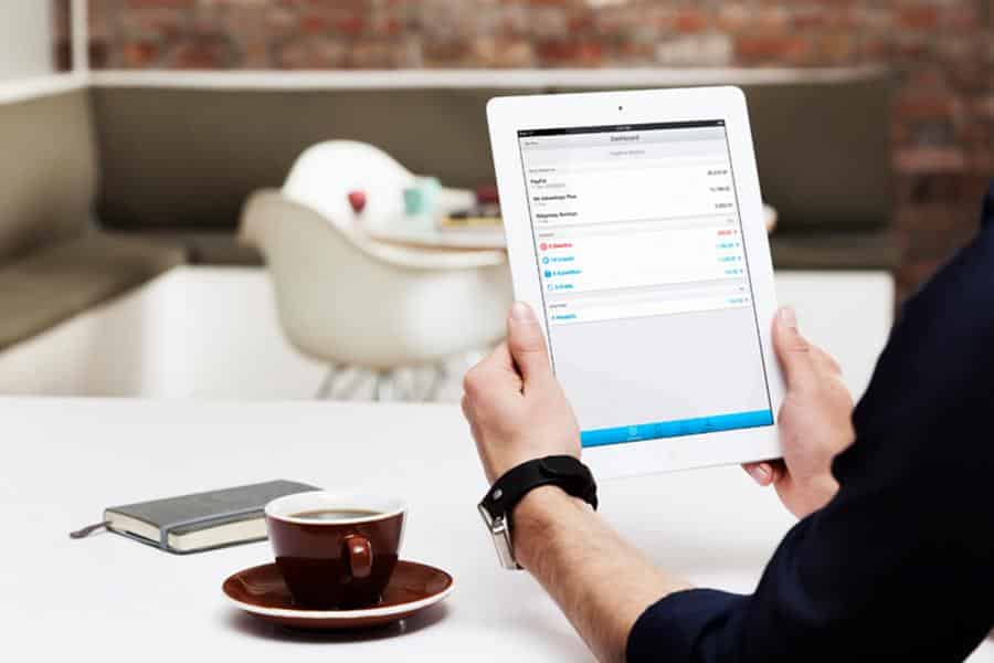 Man holding an Ipad with coffee and small notebook beside