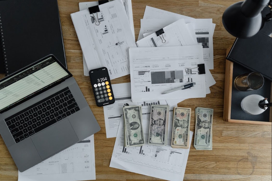 A laptop, a phone with a calculator app, bills, and several documents on a table.