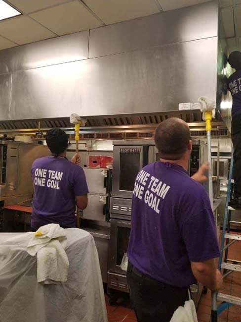 Restaurant cleaners use equipment to remove grease from a restaurant kitchen hood.
