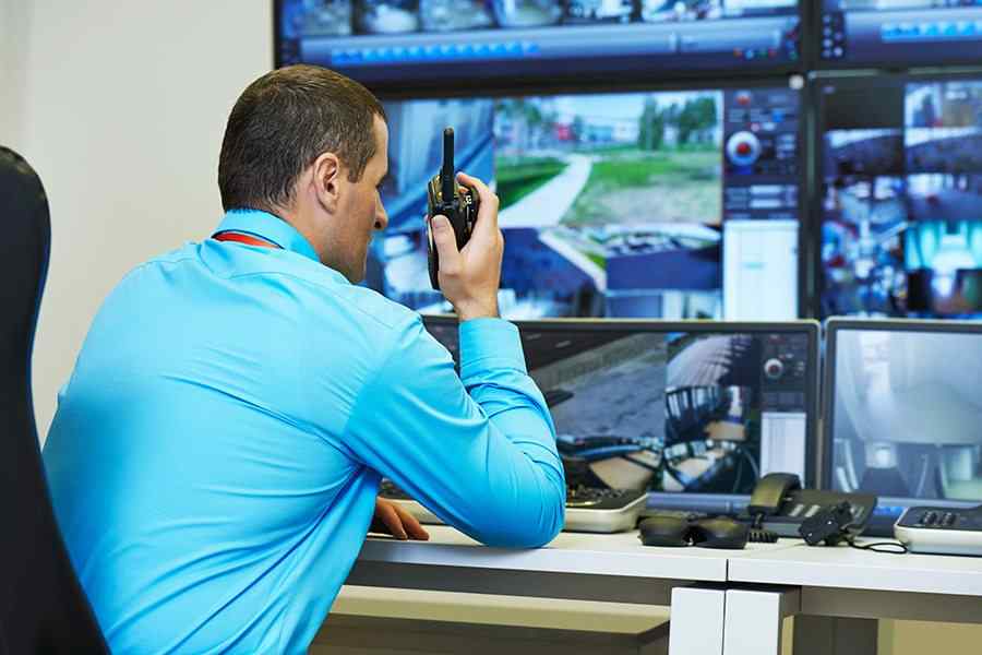 Man watching surveillance monitors and using a radio.