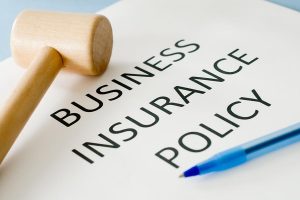 A Business Insurance Policy text, a wooden hammer and a pen.