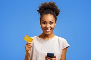 A gorgeous lady holding a credit card on her right-hand and a phone on her left hand while smiling.