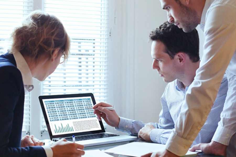 Employees are gathered in front of a laptop for discussions while data showing on the screen.