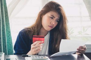 A confused woman holding a credit card and a bill in her other hand.
