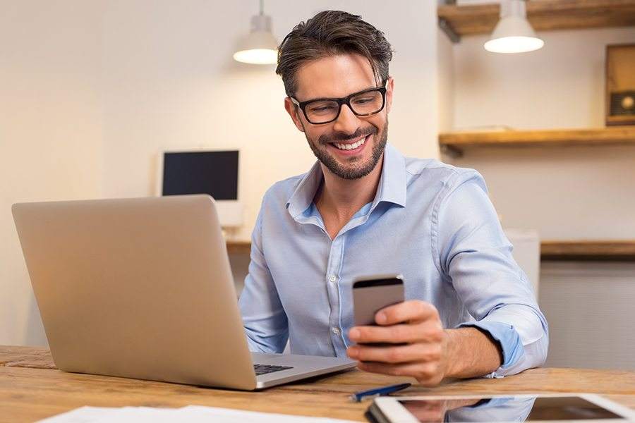 A man in his office happily reading a message on his smartphone.