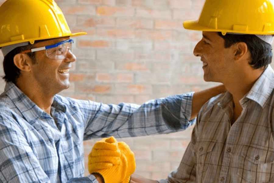 Portrait of two man wearing a hardhat while smiling to each .other.