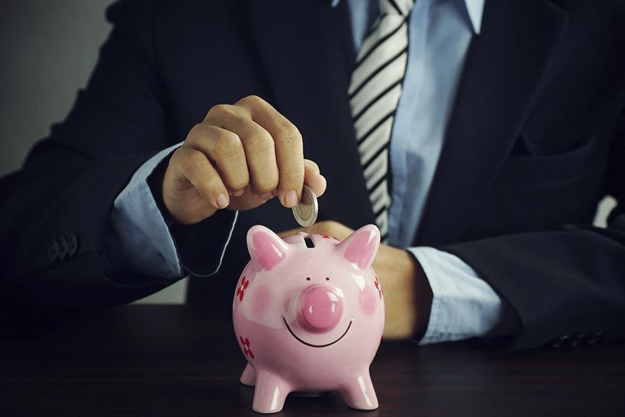 Man in business suit is holding coin and piggy bank.