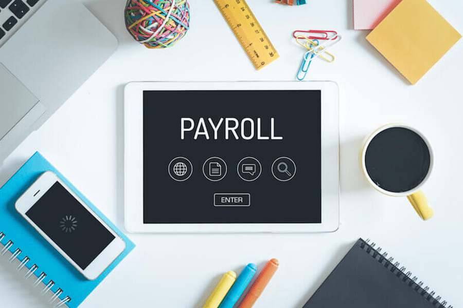 Payroll on a tablet and other items seen in a workplace on the table.