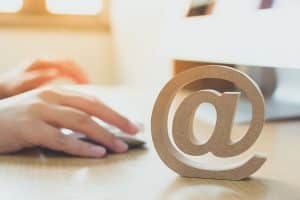 A person using computer sending message with wooden email address symbol.
