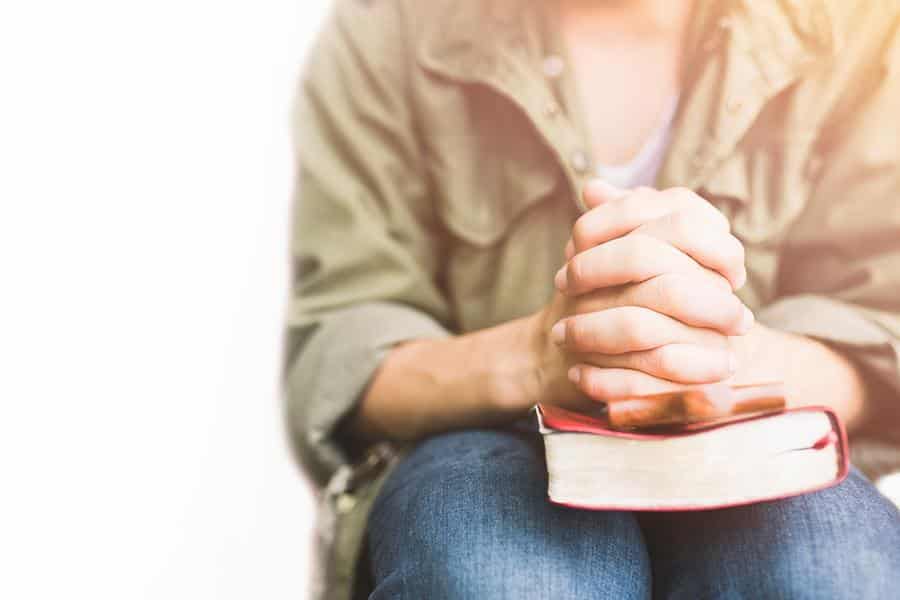 Woman with a book on her lap while holding her hands.