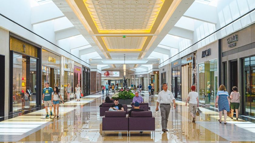 Showing shoppers walk through a shopping center full of stores.