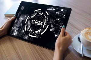 Hand holding a tablet with CRM on screen.