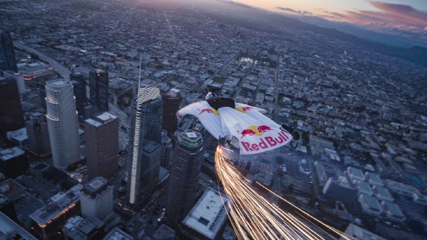 A stunt person wearing Red Bull-branded wingsuit jumping over the Los Angeles skyline.