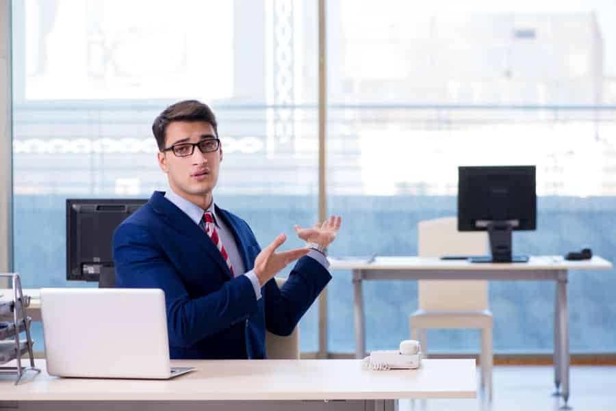 Office guy pointing to the desk of an absentee colleague.