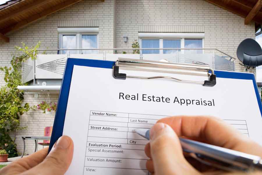 Close-up Of Person Hand Filling Real Estate Appraisal Document