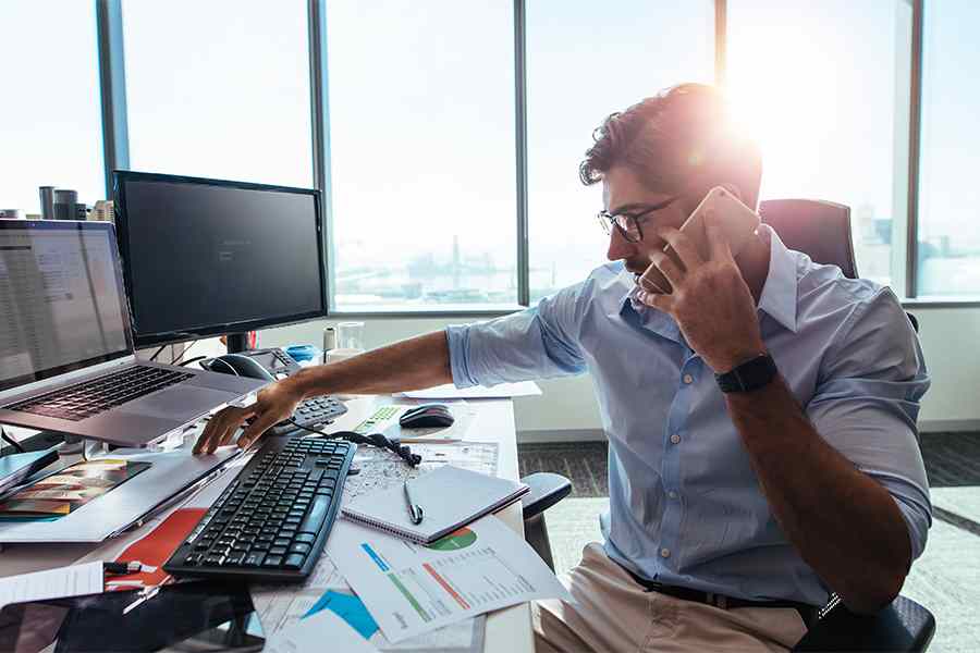 Businessman talking on mobile phone while working on computer at his desk
