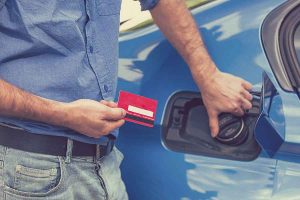 Man holding a fuel card beside a blue car.