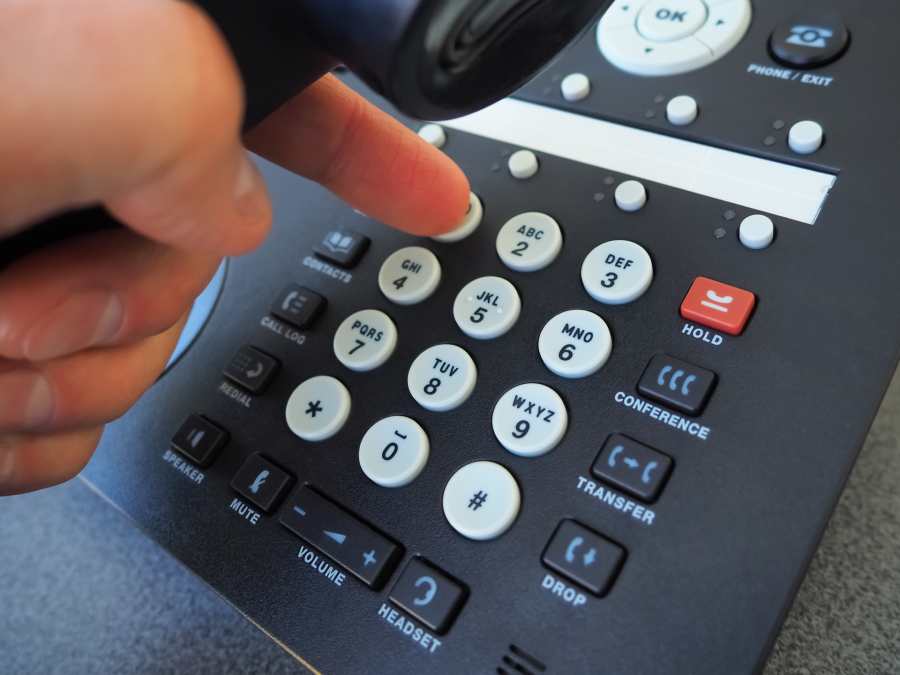 Closeup of male hand holding telephone receiver while dialing a telephone number to make a call.