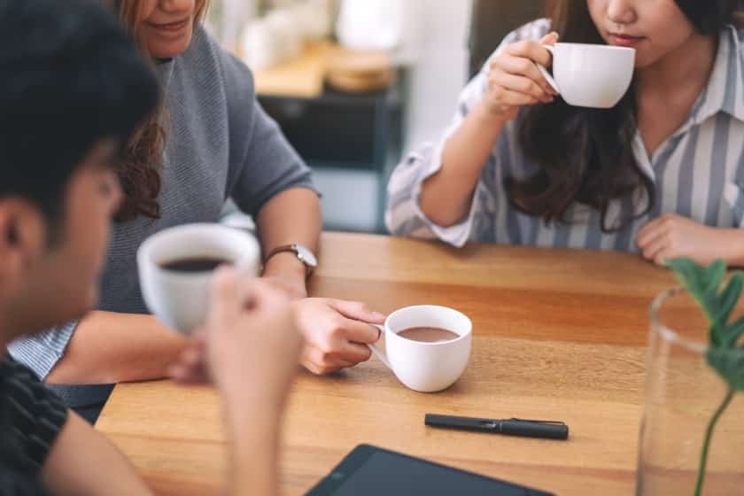 three people drinking coffee while meeting in office