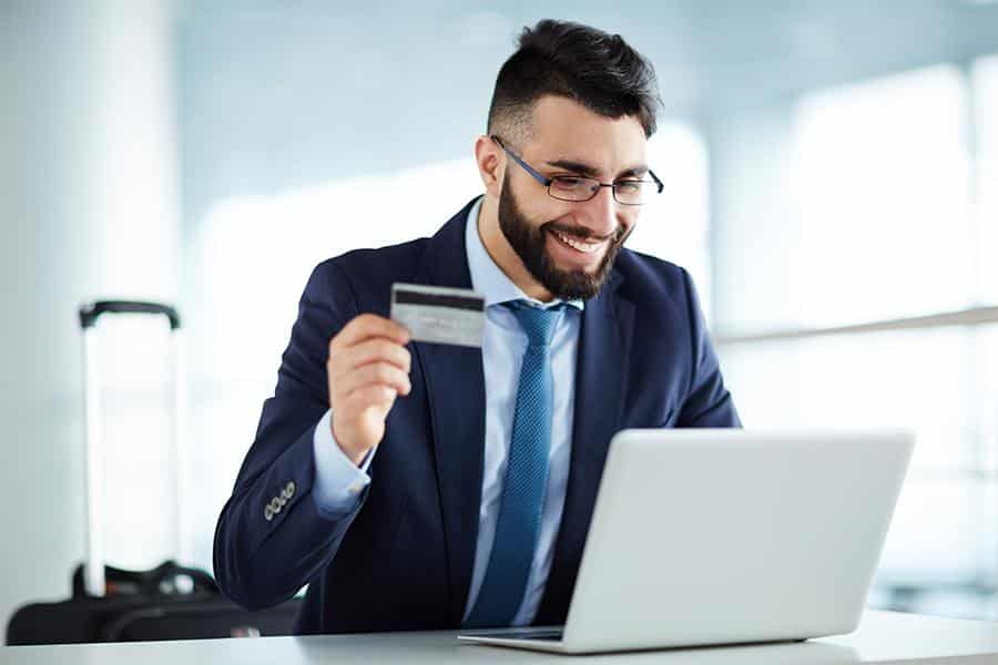 Happy businessman holding credit card on his right hand while buying online.