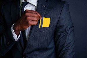 Man in business suit placing a yellow credit card on his pocket.