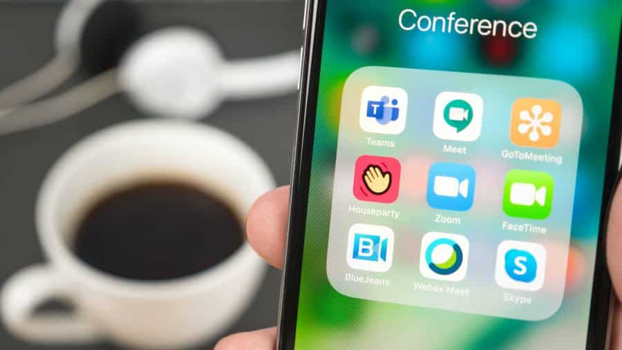 Video call conference mobile apps grouped in icon folder with a cup of coffee in the background.
