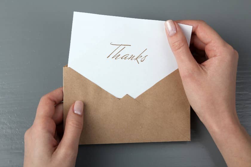 Woman's hands opening a letter with the word "Thanks" written on it.