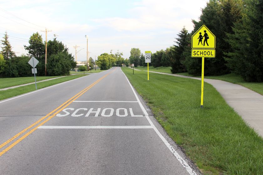 School zone sign in a yellow post and one written on the road.