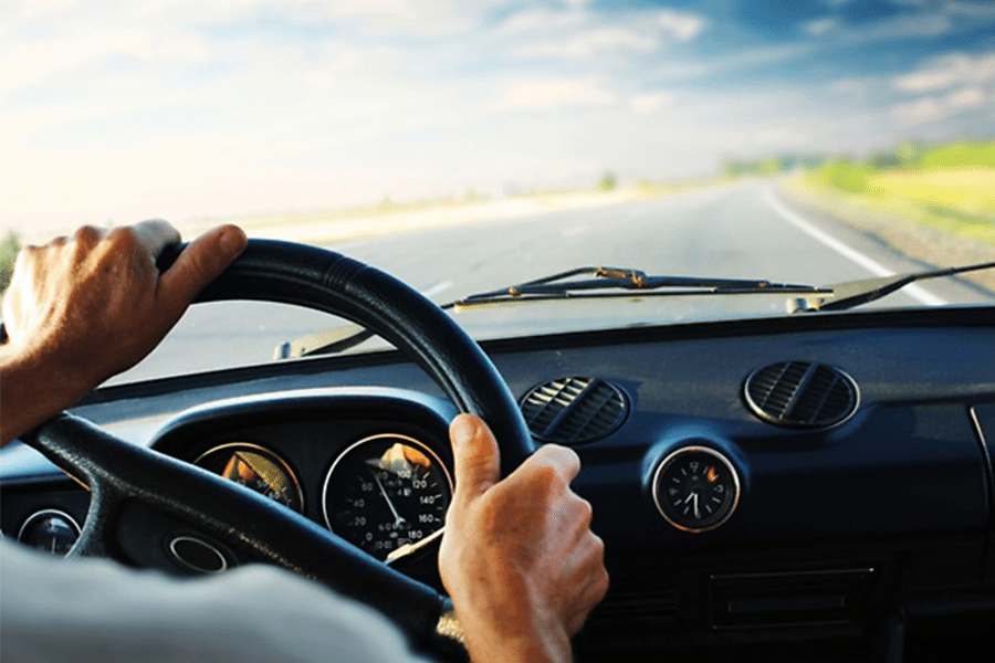 Close up shot of a man's hand gripping steering wheel while driving.