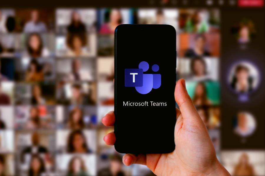Smartphone with Microsoft teams logo on its screen and headshots of meeting participants in the background.