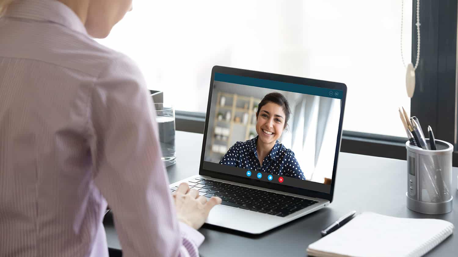 Girl communicate with friend on-line by video call, pc screen view over female shoulder.