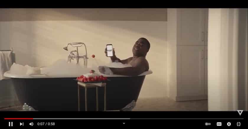 Tracy Morgan is inside a bathtub holding up the Rocket Mortgage logo on his phone.