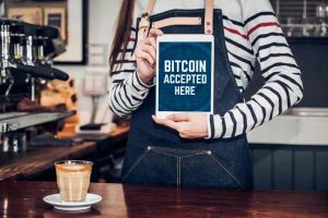 Showing a staff holding a tablet with Bitcoin accepted here sign.