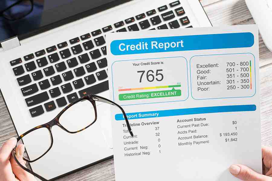 A lady looking at credit report over laptop next to glasses.