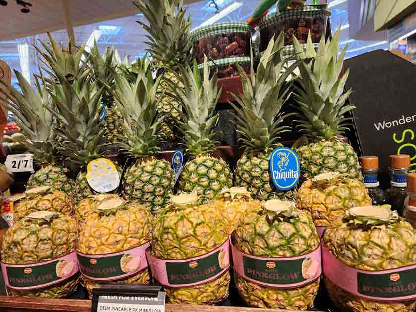 Pineapples with unusual packaging placed in front of standard fruit.