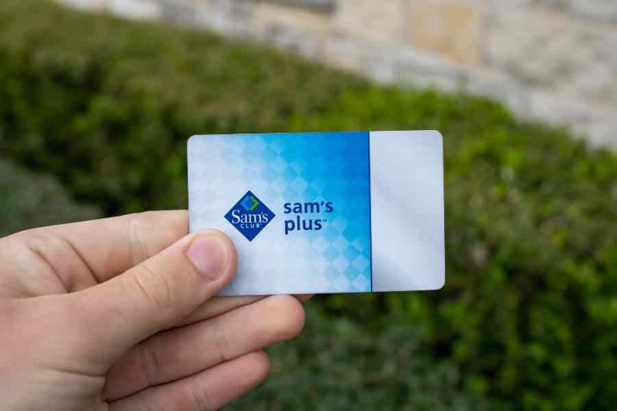 A hand holds a Sam's Club Plus Member membership card, which gives users access to Sam's Club warehouse shopping, rewards, cheap food courts.