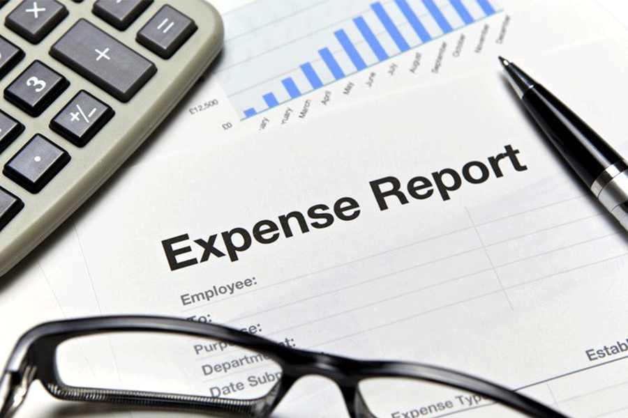 An expense report with a calculator, pen and reading glasses.
