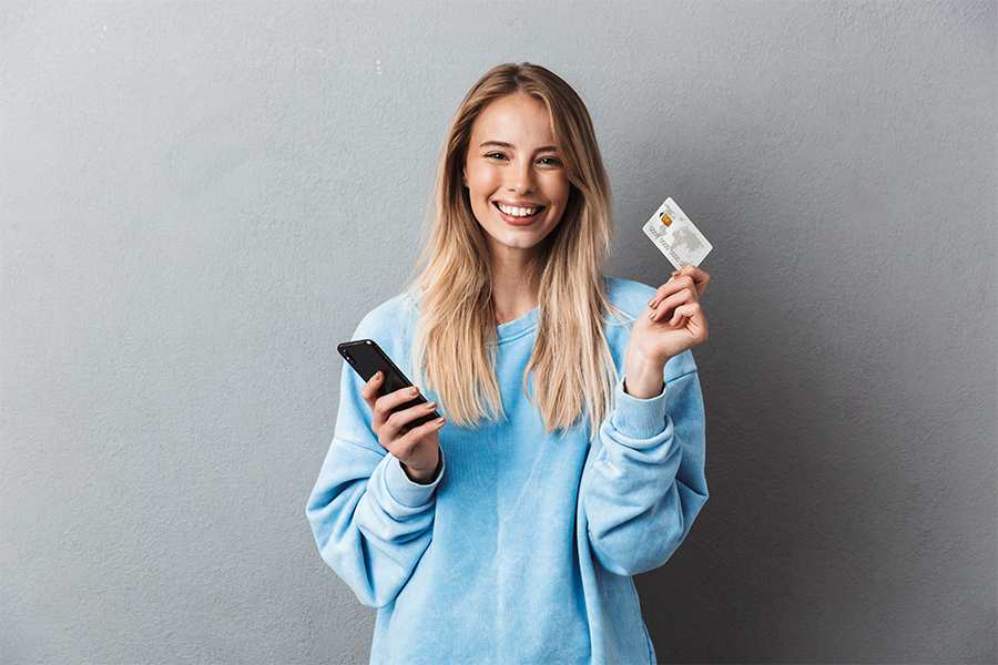 A smiling young lady holding phone and a card.