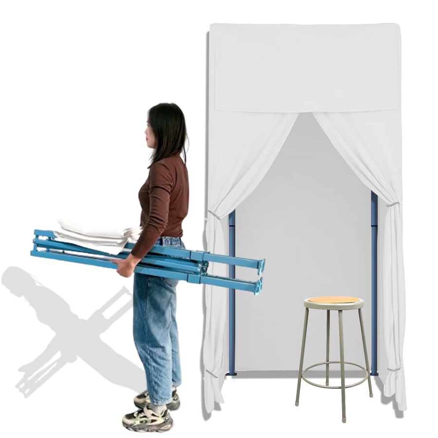 White mobile fitting room product image with room set up in background and a woman carrying it while collapsed in the foreground.