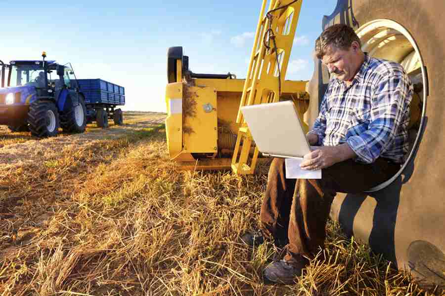 Businessman working on his laptop while sitting on a tractor's wheel
