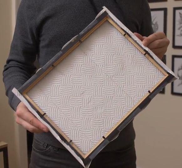 Showing a man holding a paper towel wrapped around an empty picture frame.