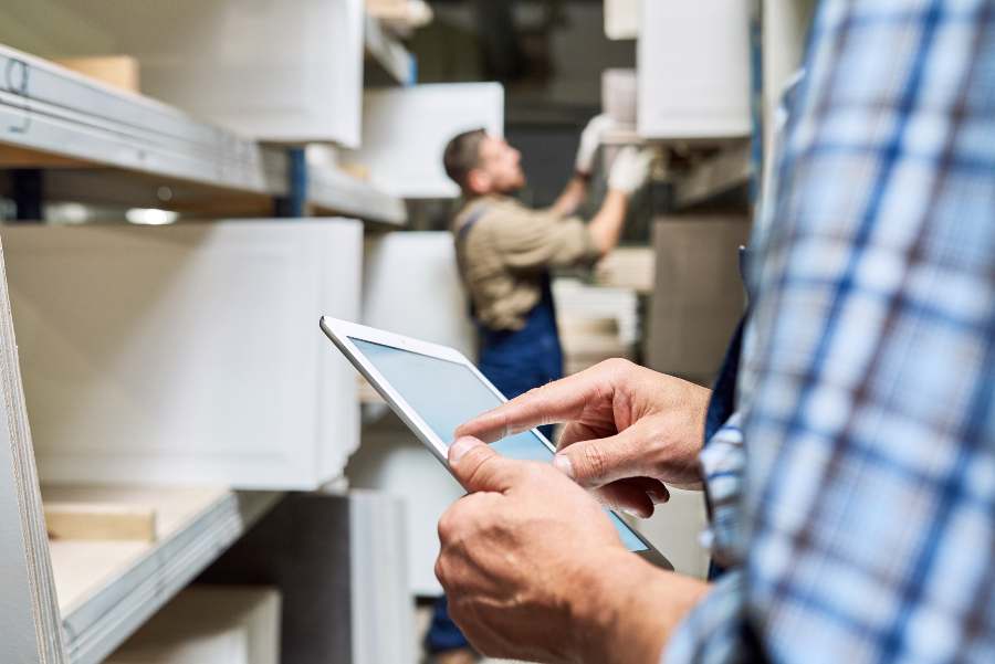Worker holding digital tablet while doing inventory in factory storage room.