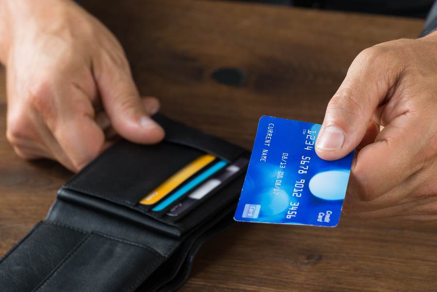 Man's hand holding a wallet and credit card for payment.