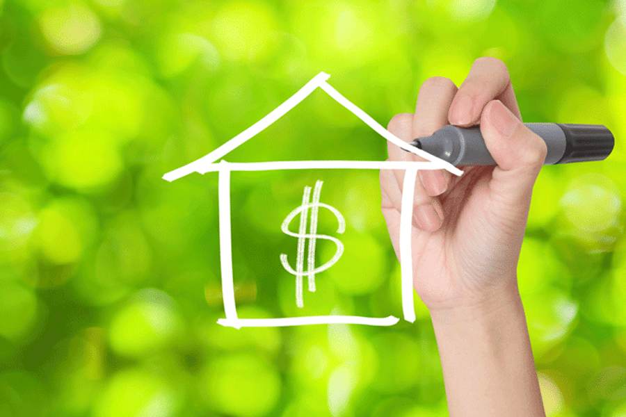 A hand with a marker drawing a house with a dollar sign on it.