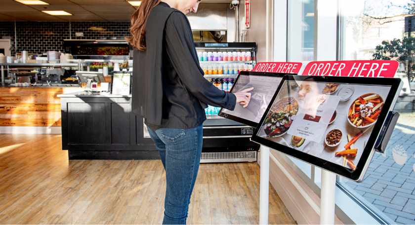 Showing a woman using self-ordering kiosk.