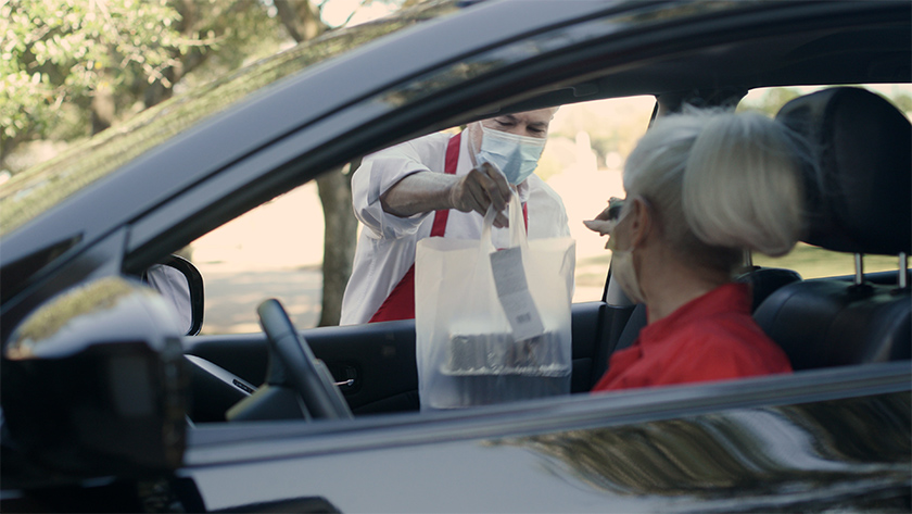 Focus on restaurant worker as he puts this woman's curbside food order through the passenger window of her car.