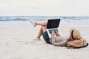 Young woman working, using laptop computer on a beach.