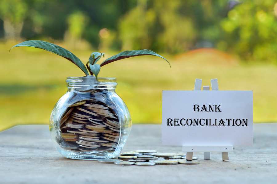 Money in glass container with tree and white board written Bank Reconciliation.