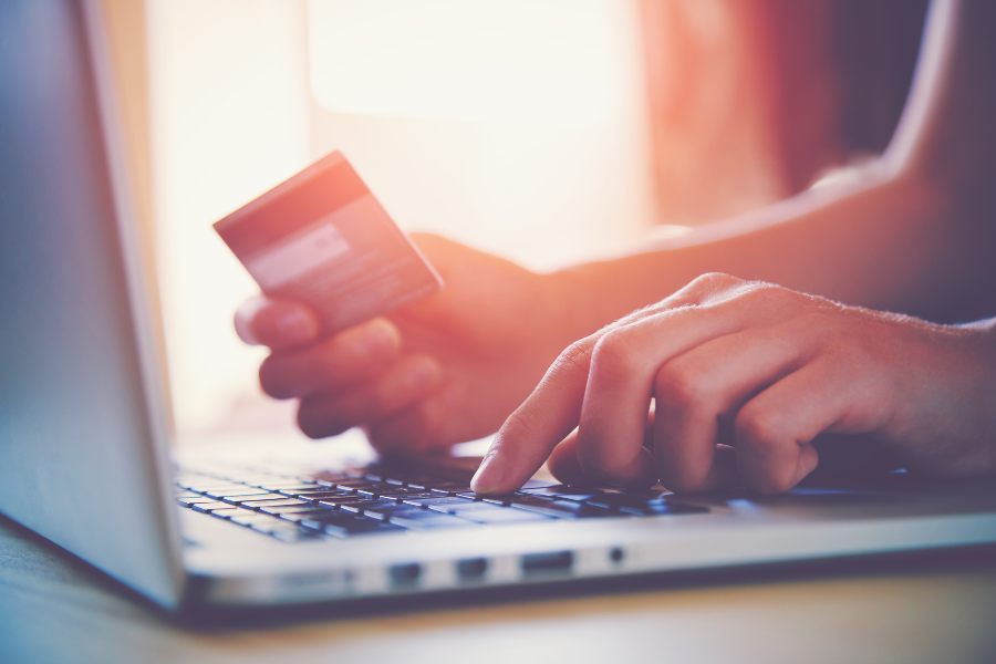 Hand holding a credit card while using a laptop.